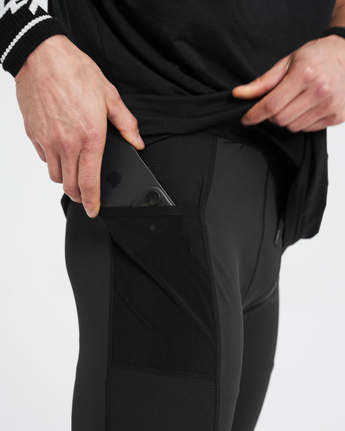 Man wearing black cargo half tights on a plain white background | 247 Cargo Half Tight in Jet Black | Training shorts with stretch ripstop side panelling | 247 Shorts | Represent Clo