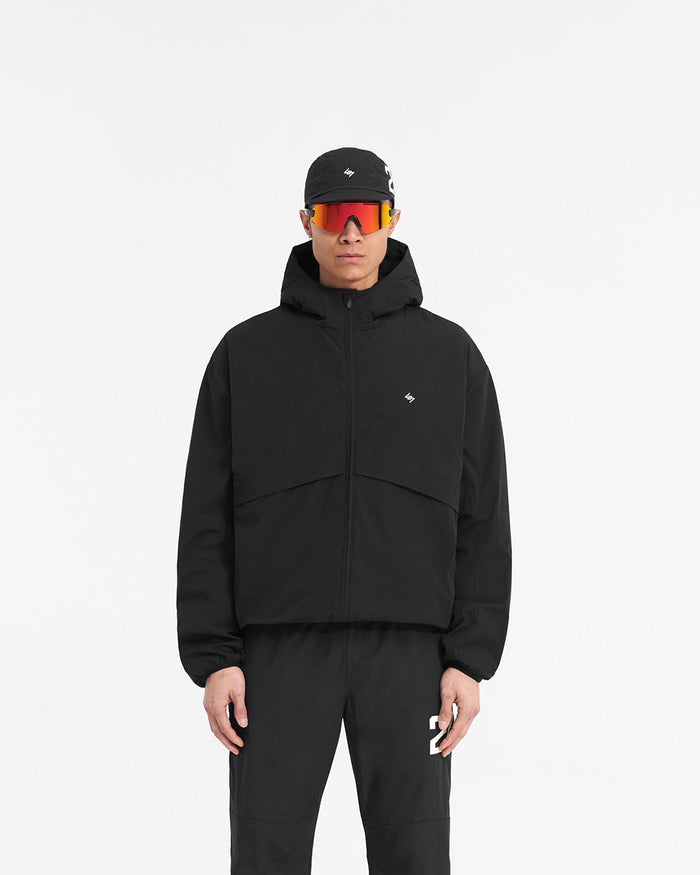 Man wearing a black hooded training jacket on a plain white background | 247 Hooded Training Jacket in Jet Black | Nylon jacket with DWR coating and adjustable hem | 247 Outerwear | Represent Clo