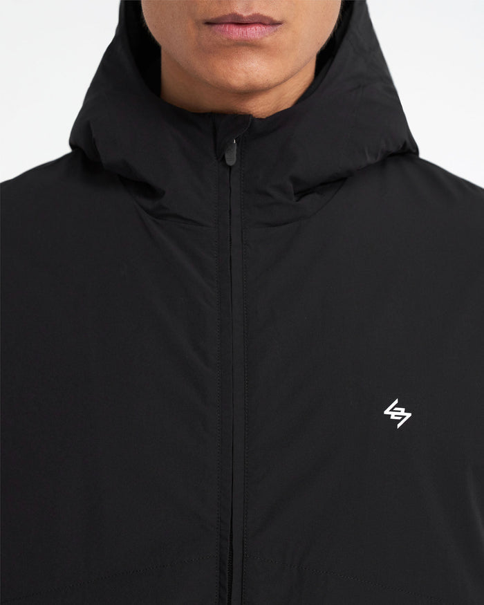 Man wearing a black hooded jacket on a plain white background | 247 Hooded Training Jacket in Jet Black | Nylon training jacket with DWR coating | 247 Outerwear | Represent Clo