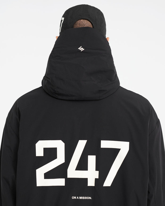 Man wearing a black hooded nylon jacket on a plain white background | 247 Hooded Training Jacket in Jet Black | Oversized fit nylon outerwear with DWR coating | 247 Outerwear | Represent Clo