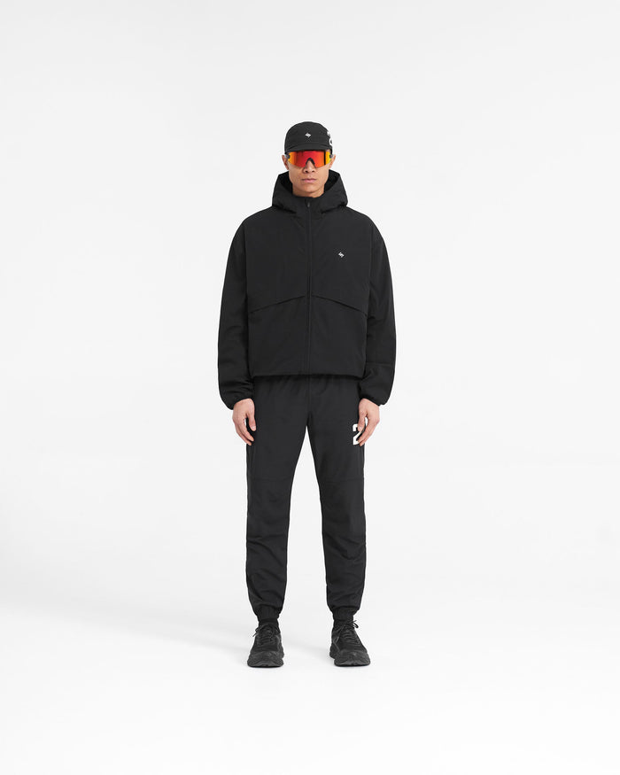 Man wearing a black hooded training jacket on a plain white background | 247 Hooded Training Jacket in Jet Black | Nylon jacket with 4-way stretch and DWR coating | 247 Outerwear | Represent Clo