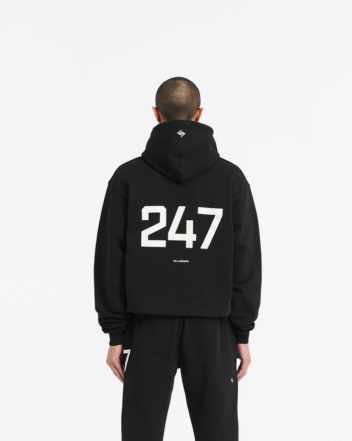 Man wearing a black oversized hoodie on a plain white background | 247 Oversized Hoodie in Jet Black | Oversized fit hoodie with ribbed cuffs | 247 Hoodies | Represent Clo