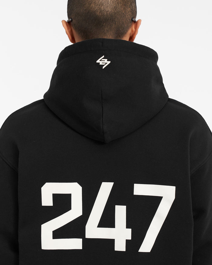 Man wearing an oversized black hoodie on a plain white background | 247 Oversized Hoodie in Jet Black | Oversized hoodie with ribbed hem and cuffs | 247 Hoodies | Represent Clo
