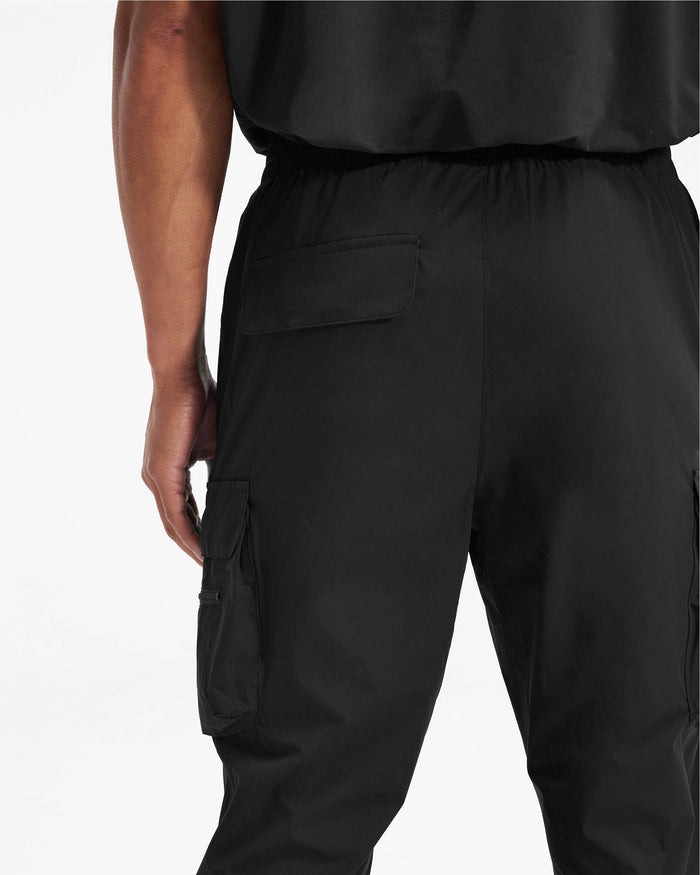 Man wearing black pants on a plain white background | 247 Pant in Black | Versatile cargo pants with technical 4-way stretch and zip side pockets | 247 Pants | Represent Clo
