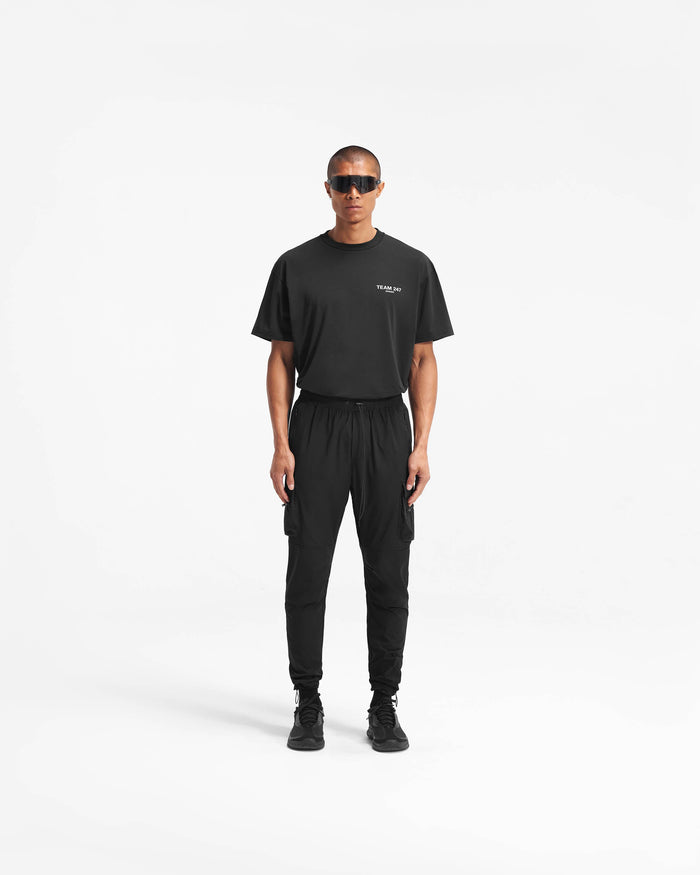 Man wearing black cargo pants on a plain white background | 247 Pant in Black | Versatile nylon cargo pants with zip pockets | 247 Pants | Represent Clo