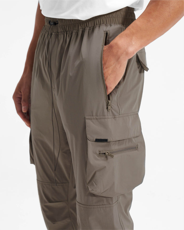 Man wearing olive cargo pants on a plain white background | 247 Pant in Olive | Cargo pants with 4-way stretch and zip side pockets | 247 Pants | Represent Clo