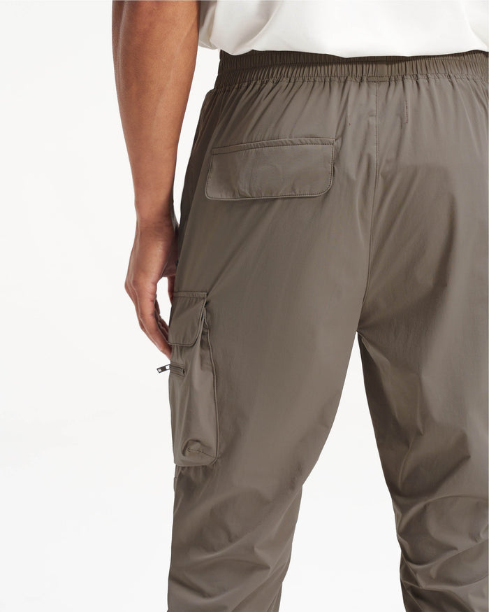 Man wearing olive pants on a plain white background | 247 Pant in Olive | Cargo pants with elasticated drawstring waistband and zip pockets | 247 Pants | Represent Clo