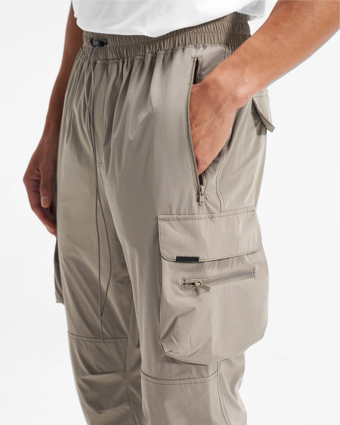 Man wearing taupe pants on a plain white background | 247 Pant in Taupe | Versatile cargo pants with spacious pockets and adjustable details | 247 Pants | Represent Clo