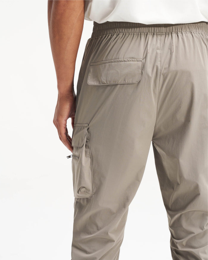 Man wearing taupe cargo pants on a plain white background | 247 Pant in Taupe | Versatile cargo pants with 4-way stretch and zip pockets | 247 Pants | Represent Clo