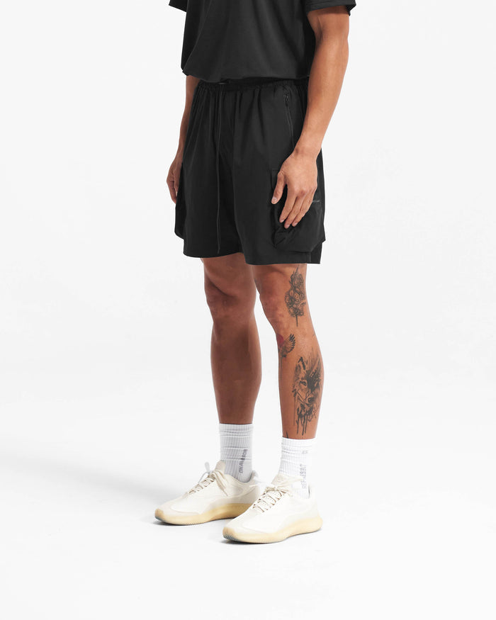 Man wearing black combat shorts on a plain white background | 247 Shorts in Black | Mens combat shorts with cargo leg pockets and elasticated drawstring waist | 247 Shorts | Represent Clo