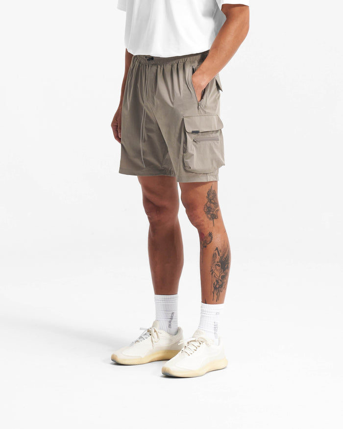 Man wearing taupe shorts on a plain white background | 247 Shorts in Taupe | Combat shorts with cargo leg pockets and zip side pockets | 247 Shorts | Represent Clo