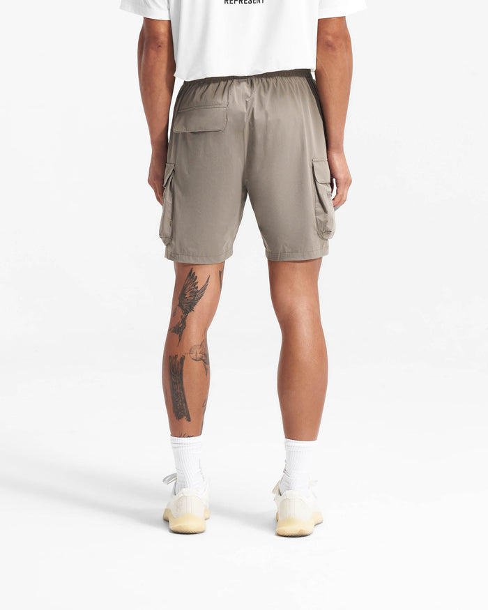 Man wearing taupe shorts on a plain white background | 247 Shorts in Taupe | Mens combat shorts with cargo leg pockets and zip pockets | 247 Shorts | Represent Clo