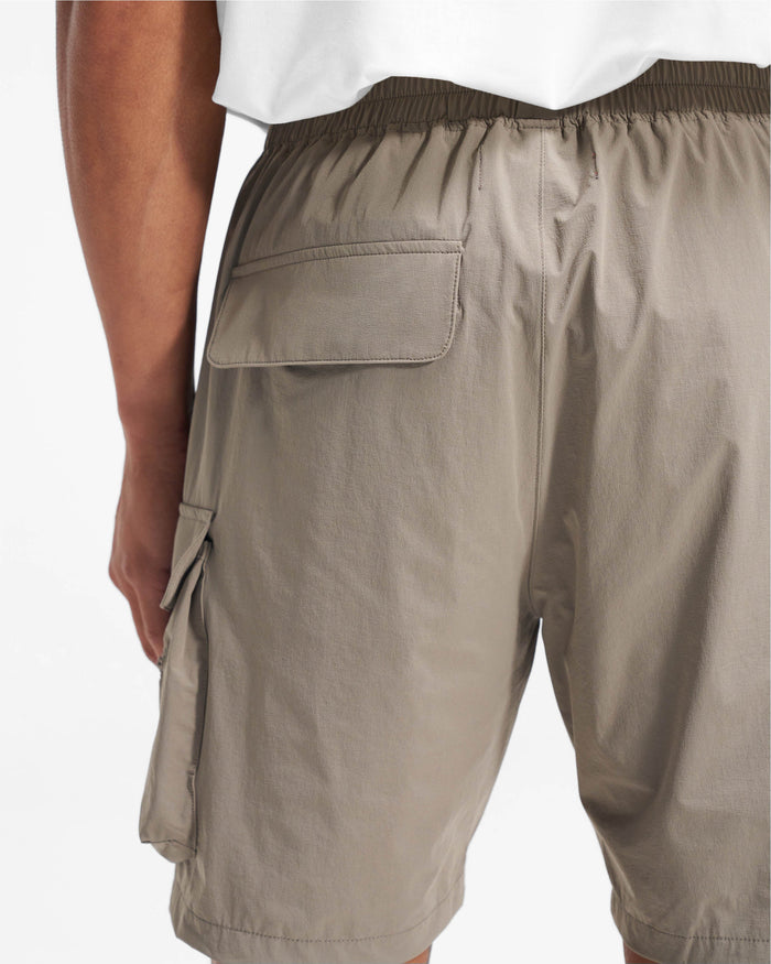 Man wearing taupe nylon shorts on a plain white background | 247 Shorts in Taupe | Mens combat shorts with cargo and zip pockets | 247 Shorts | Represent Clo