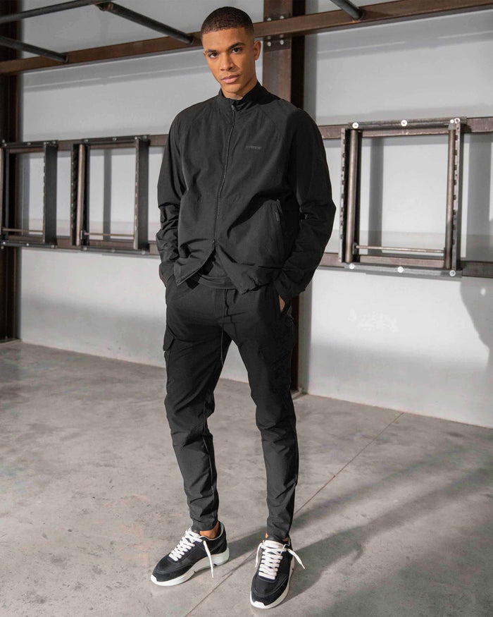 Man wearing black pants on a plain white background | 247 Zip Pant in Black | Slim taper pants with cargo and zip pockets | 247 Pants | Represent Clo