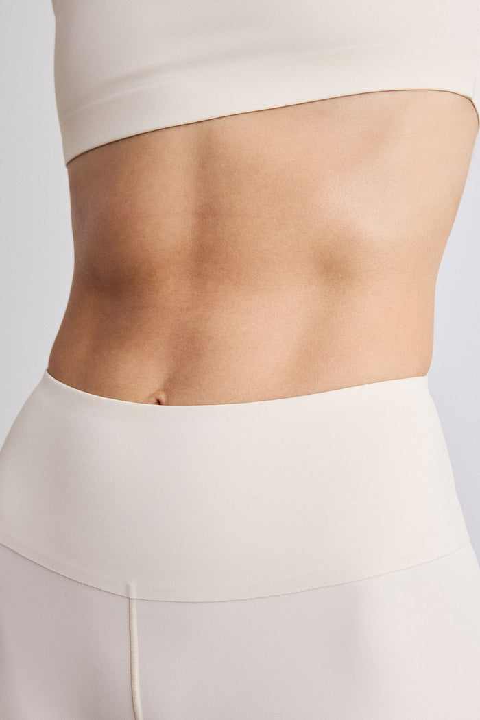 Close-up of a model's midsection wearing a cream-colored sports bra and matching high-waisted bike shorts against a light gray background.