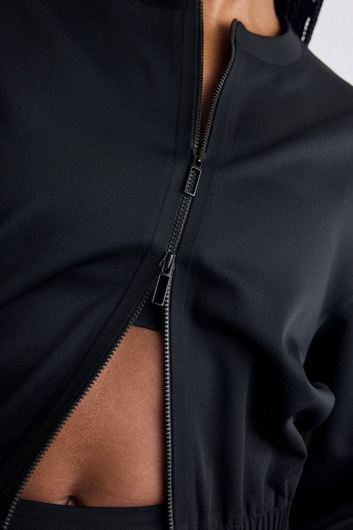 Close-up of a black zip-front jacket worn by a model, showing the zipper detail.