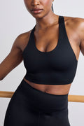 A close-up of a model wearing a black athletic sports bra and matching black high-waisted leggings against a light gray background.