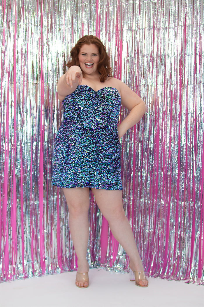 SC8157, plus size short sequin party dress by Sydney's Closet. Front view. A fully multidimensional sequin fabric in the color Galaxy, a mixture of blues and purples. Sweetheart neckline, ruched skirt and long invisible center back zipper. Available in Galaxy, sizes 14-24. Model is 5'9.