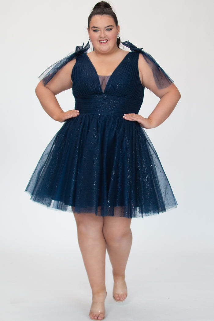 Short A-line plus size flowy party dress SC8153 by Sydney's Closet in the color Admiral blue. Front view. Layers of dense sparkle tulle and a satin lining. V-neckline with thick bra-friendly straps and detachable bows at the top of the shoulder. Pleated bodice and 3 inch pleated waistband. Pockets and long invisible center back zipper. Available in Shamrock green, Admiral blue and firecracker red, sizes 14-32.
Model is 5'9.