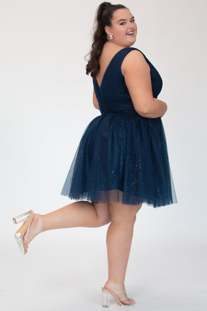 Short A-line plus size flowy party dress SC8153 by Sydney's Closet in the color Admiral blue. Back view. Layers of dense sparkle tulle and a satin lining. V-neckline with thick bra-friendly straps and detachable bows at the top of the shoulder. Pleated bodice and 3 inch pleated waistband. Pockets and long invisible center back zipper. Available in Shamrock green, Admiral blue and firecracker red, sizes 14-32.
Model is 5'9.
