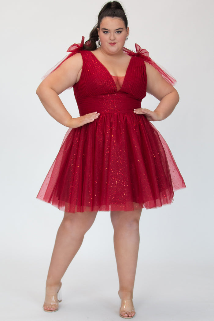 Short A-line plus size flowy party dress SC8153 by Sydney's Closet in the color Firecracker red. Front view. Layers of dense sparkle tulle and a satin lining. V-neckline with thick bra-friendly straps and detachable bows at the top of the shoulder. Pleated bodice and 3 inch pleated waistband. Pockets and long invisible center back zipper. Available in Shamrock green, Admiral blue and firecracker red, sizes 14-32.
Model is 5'9.