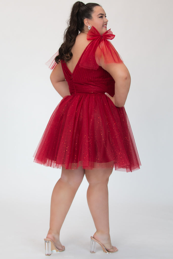 Short A-line plus size flowy party dress SC8153 by Sydney's Closet in the color Firecracker red. Back view. Layers of dense sparkle tulle and a satin lining. V-neckline with thick bra-friendly straps and detachable bows at the top of the shoulder. Pleated bodice and 3 inch pleated waistband. Pockets and long invisible center back zipper. Available in Shamrock green, Admiral blue and firecracker red, sizes 14-32.
Model is 5'9.