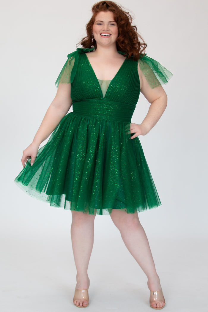 Short A-line plus size flowy party dress SC8153 by Sydney's Closet in the color Shamrock green. Front view. Layers of dense sparkle tulle and a satin lining. V-neckline with thick bra-friendly straps and detachable bows at the top of the shoulder. Pleated bodice and 3 inch pleated waistband. Pockets and long invisible center back zipper. Available in Shamrock green, Admiral blue, Firecracker red and Onyx black in sizes 14-32. Model is 5'9.