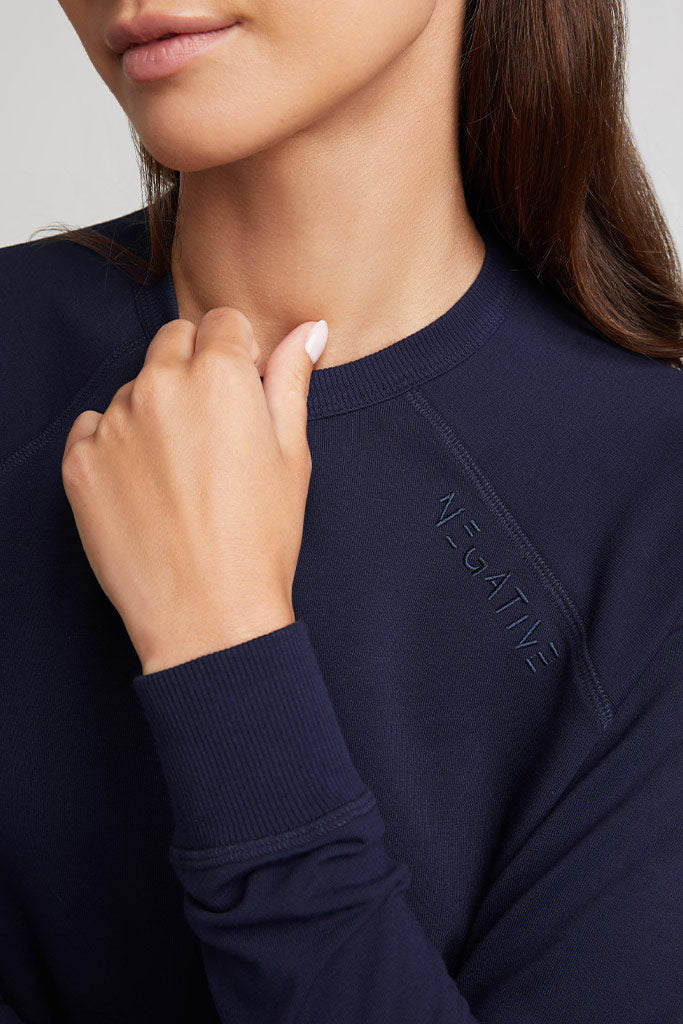 Navy crewneck sweatshirt close-up, ribbed collar and stitched logo detail at chest