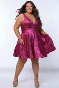 Plus-size model wearing a sleeveless a-line mini dress in a vibrant metallic fuchsia pink knit fabric. The dress features a deep V-neckline, fitted waistband, and a full flared skirt with subtle pleating. She is styled with long wavy dark brown hair, hoop earrings, and nude platform ankle-strap heels, posing against a light gray studio background while showing off the pockets in the skirt.

Sydney's Closet SC8175 in magenta