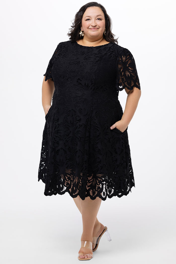 Plus size little black dress made of Guipure lace. Short sleeves, scoop neckline and center back zipper. CE2601 available in sizes 14-24 in black. Celebrations by Sydney's Closet.