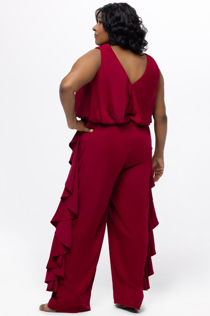 Celebrations by Sydney's Closet Style CE2615 in cherry red.

One-piece crepe satin jumpsuit with ruffled on outer pants seams. Bra-friendly straps, blouson bodice and wide leg pants. Center back zipper and scoop neckline.