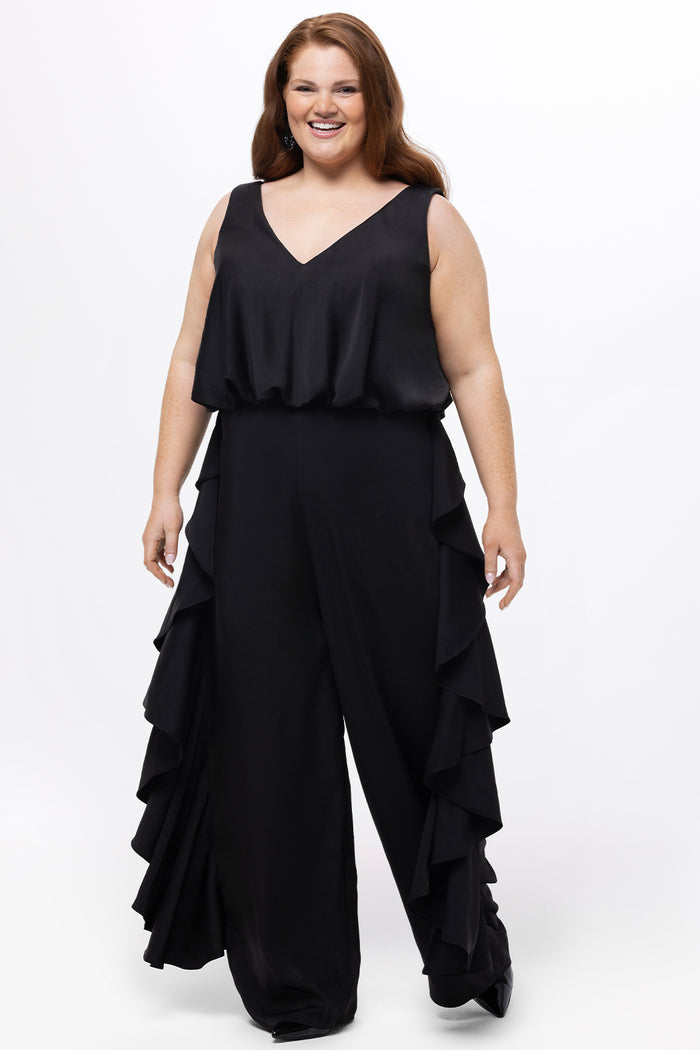 Celebrations by Sydney's Closet Style CE2615 in Black.

One-piece crepe satin jumpsuit with ruffled on outer pants seams. Bra-friendly straps, blouson bodice and wide leg pants. Center back zipper and scoop neckline.