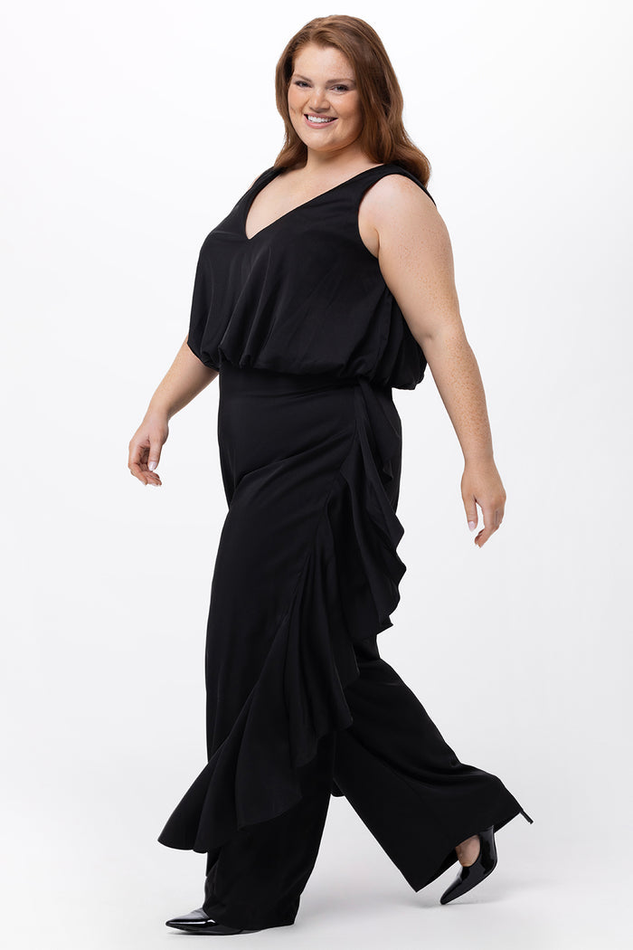 Celebrations by Sydney's Closet Style CE2615 in Black.

One-piece crepe satin jumpsuit with ruffled on outer pants seams. Bra-friendly straps, blouson bodice and wide leg pants. Center back zipper and scoop neckline.