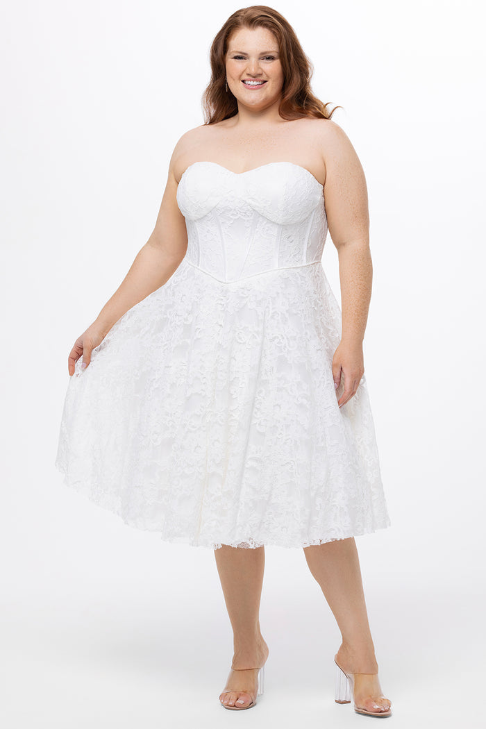 Celebrations by Sydney's Closet Style CE2613 in white. 

Plus size strapless white tea-length dress with sweetheart neckline, exposed corset boning on bustier bodice and tea-length skirt in all over stretch lace.