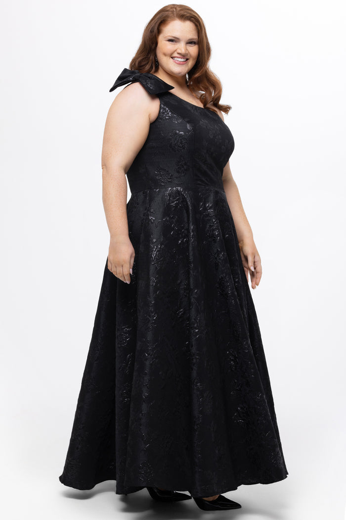 Celebrations by Sydney's Closet Style CE2614 in Black

Plus size maxi length formal dress. One-shoulder neckline with detachable bow at high point of shoulder, natural waistline and A-line skirt with pockets. 

Black floral brocade fabric.
