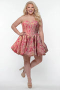 Plus-size model wearing a strapless a-line mini dress in pink floral brocade with metallic gold accents. The dress features a structured corset-style bodice with a strapless sweetheart neckline and a voluminous bubble hem skirt. She is styled with long wavy blonde hair, statement pink crystal earrings, and nude platform ankle-strap heels, posing against a light gray studio background.

Sydney's Closet SC8177 in pink floral
