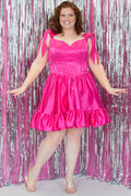 SC8152 by Sydney's Closet. Lipstick pink, front view. A short satin party dress with a 5 inch ruffle at the hem and decorative bows at the top of the shoulder. A lace up back, exposed boning and sweetheart neckline. With a basque waist and lace up back. Available in Sapphire blue and Lipstick pink, sizes 14-28. 
Model is 5'9.