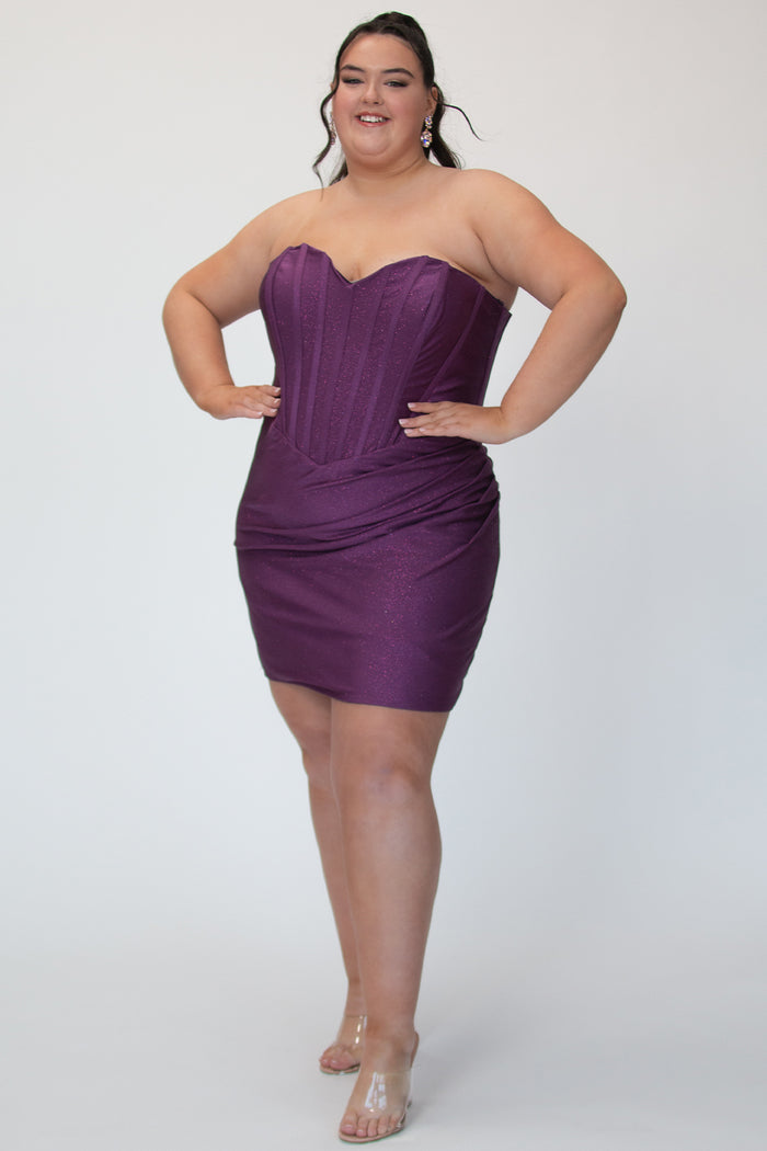 Short fitted purple party dress SC8143 by Sydney's Closet. Front view.  Strapless, exposed boning basque waist and ruched fitted skirt in shimmer stretch knit. Long invisible center back zipper. Availability in black, purple, red, ivory, green and royal. Model in picture is 5'9.