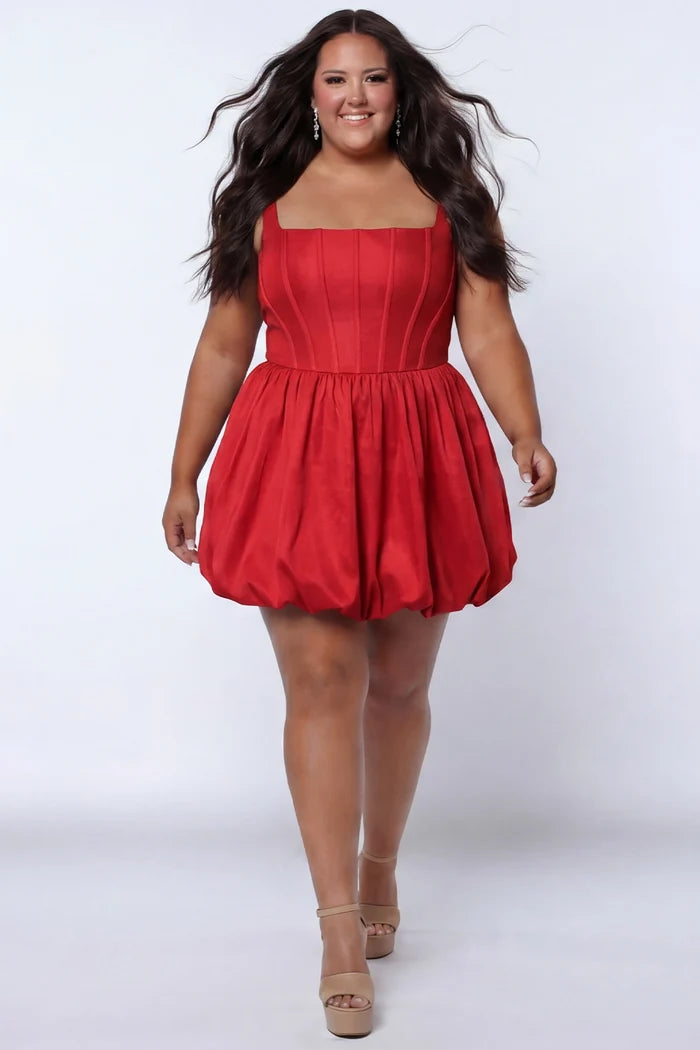 Plus-size model wearing a red sleeveless taffeta mini dress with a square neckline, structured corset-inspired bodice with exposed boning, and voluminous bubble hem skirt. She is styled with long flowing brown hair, drop earrings, and nude platform ankle-strap heels, walking toward the camera against a light gray studio background. Front view.

Sydney's Closet SC8166 in red
