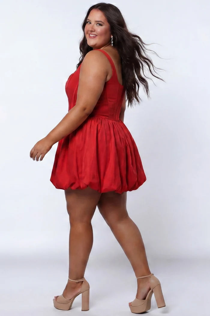 Plus-size model wearing a red sleeveless taffeta mini dress with a square neckline, structured corset-inspired bodice with exposed boning, and voluminous bubble hem skirt. She is styled with long flowing brown hair, drop earrings, and nude platform ankle-strap heels, walking to the side against a light gray studio background. Back view.

Sydney's Closet SC8166 in red