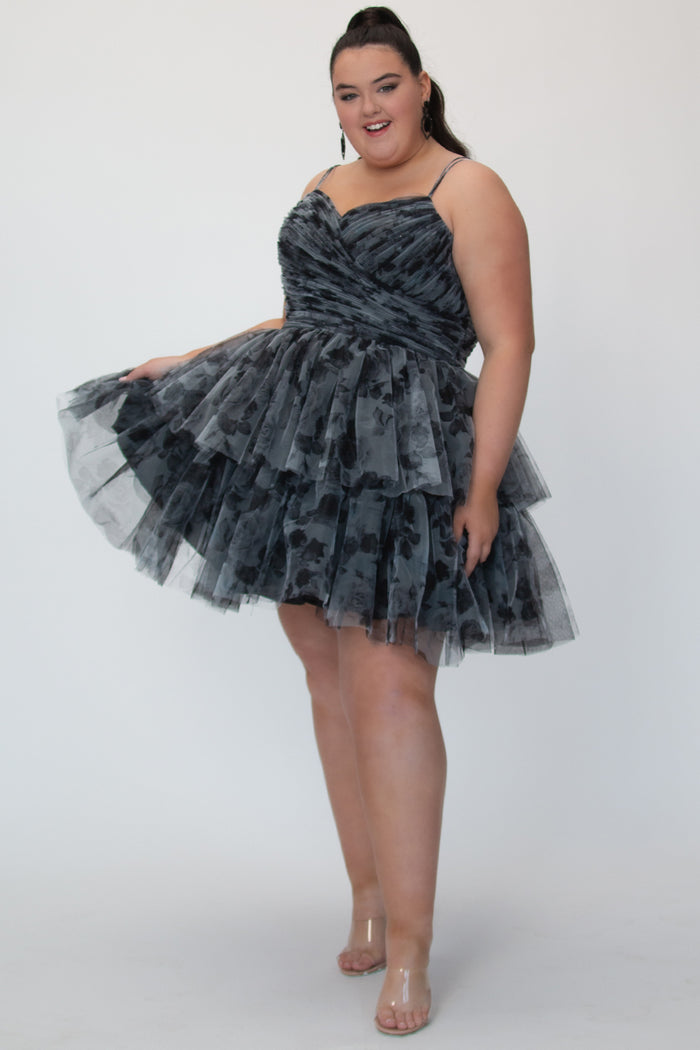 Tiered floral short party dress, SC8151 by Sydney's Closet. Front view. In the color Black/floral. Floral tulle fabric with a satin lining. Fully pleated bodice, sweetheart neckline, double spaghetti straps and a two-tiered skirt. Long invisible center back zipper. Available in blue/floral and black/floral sizes 14-32. 
Model is 5'9.