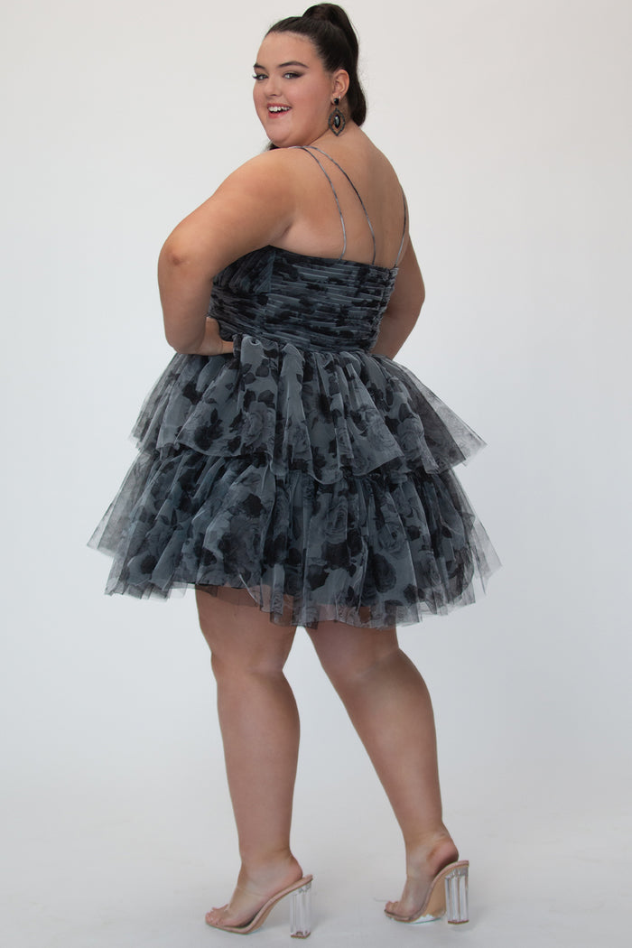 Tiered floral short party dress, SC8151 by Sydney's Closet. Back view.  In the color Black/floral. Floral tulle fabric with a satin lining. Fully pleated bodice, sweetheart neckline, double spaghetti straps and a two-tiered skirt. Long invisible center back zipper. Available in blue/floral and black/floral sizes 14-32. 
Model is 5'9.