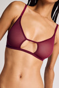 A close-up of a model wearing a sheer mesh bralette in a deep burgundy or maroon color, featuring a unique cutout design at the center of the bust.