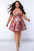 Plus-size model wearing a sleeveless a-line mini dress with a scoop neckline and metallic floral brocade pattern in fuchsia pink, gold, and champagne tones. The dress features straps, a fitted bodice and a flared skirt with soft pleats. She is styled with long flowing dark brown hair, dangling earrings, and nude platform ankle-strap heels, walking toward the camera against a light gray studio background.

Sydney's Closet SC8169 in fuchsia pink floral