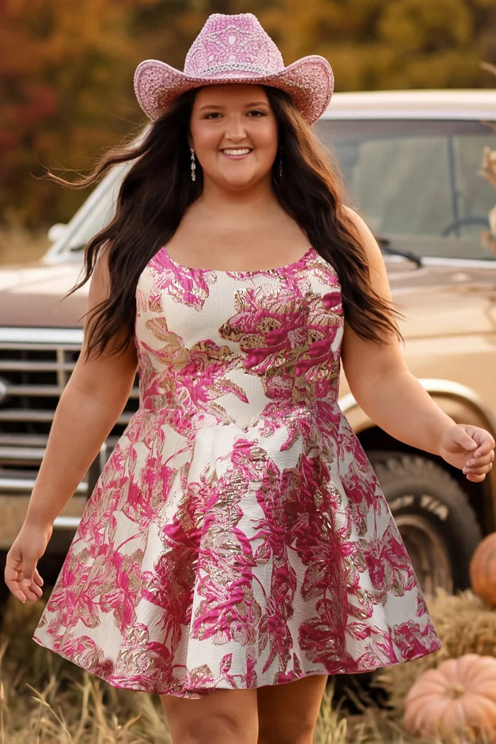 Plus-size model wearing a sleeveless a-line mini dress with a scoop neckline and metallic floral brocade pattern in shades of pink, fuchsia, and champagne. She is styled with a pink glitter cowboy hat, long flowing dark brown hair, dangling earrings, and nude ankle-strap heels. The model walks through a rustic autumn setting with pumpkins, hay bales, and a vintage tan truck in the background.

Sydney's Closet SC8169 in pink floral
