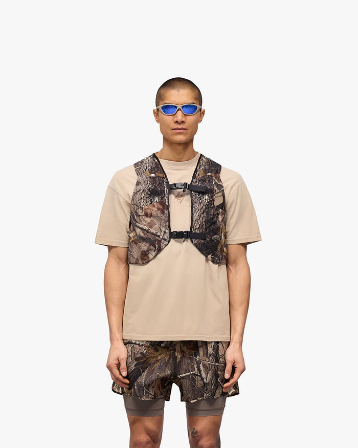 Man wearing a camo chest rig on a plain white background | Team 247 Chest Rig in Realtree | Mesh chest rig with magnetic buckles and pockets | 247 Accessories | Represent Clo