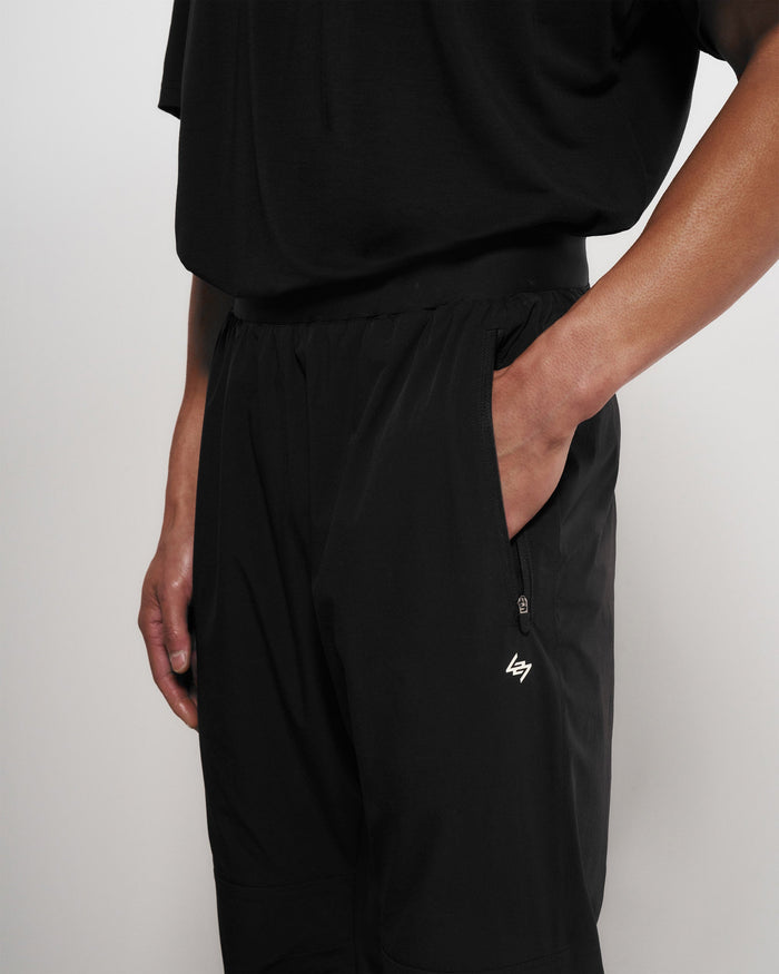 Man wearing black training pants on a plain white background | Team 247 Training Pant in Black | Nylon blend pants with zip pockets and elastic waistband | 247 Pants | Represent Clo