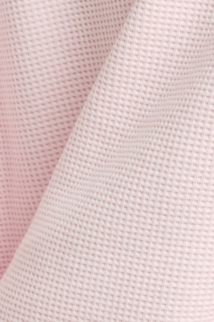 Waffle knit fabric in light pink texture close-up for track pants.