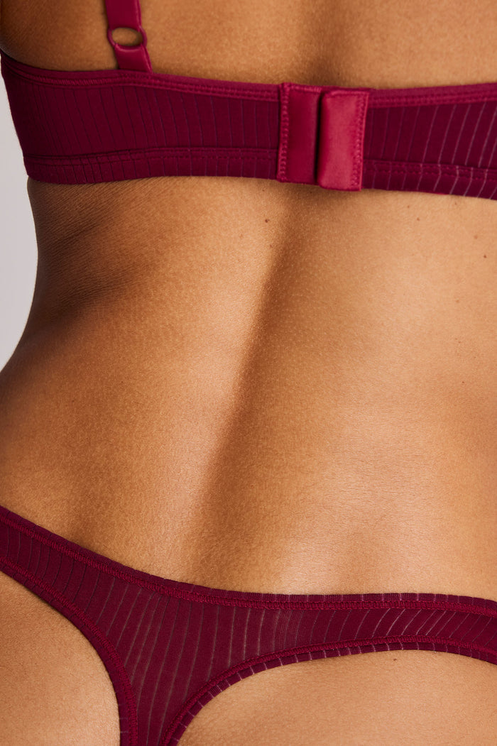 Close-up of a model's lower back wearing a deep burgundy ribbed lingerie set with a bra and thong.
