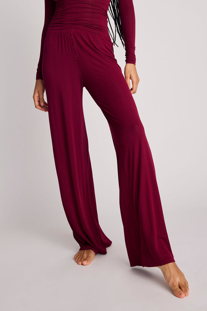 A person wearing loose, wide-leg burgundy pants with a matching long-sleeve top, shown from the chest down against a plain light gray studio background.
